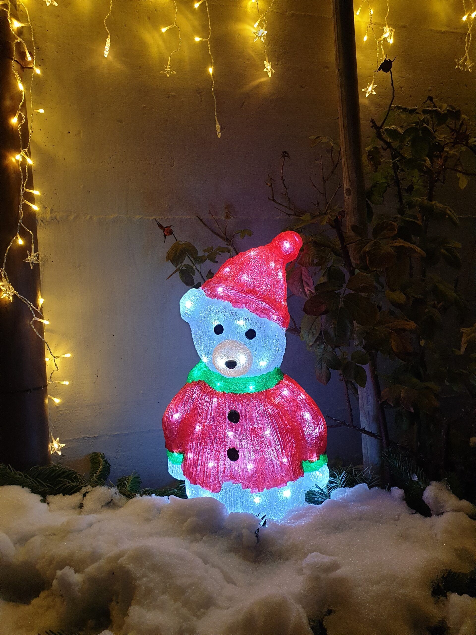 Ein Schneemann sitzt im Schnee, hinter ihm sind Weihnachtslichter zu sehen.