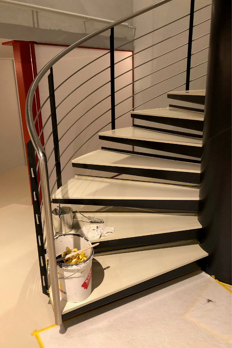 Eine Wendeltreppe mit einem Metallgeländer und einem Eimer Farbe auf dem Boden