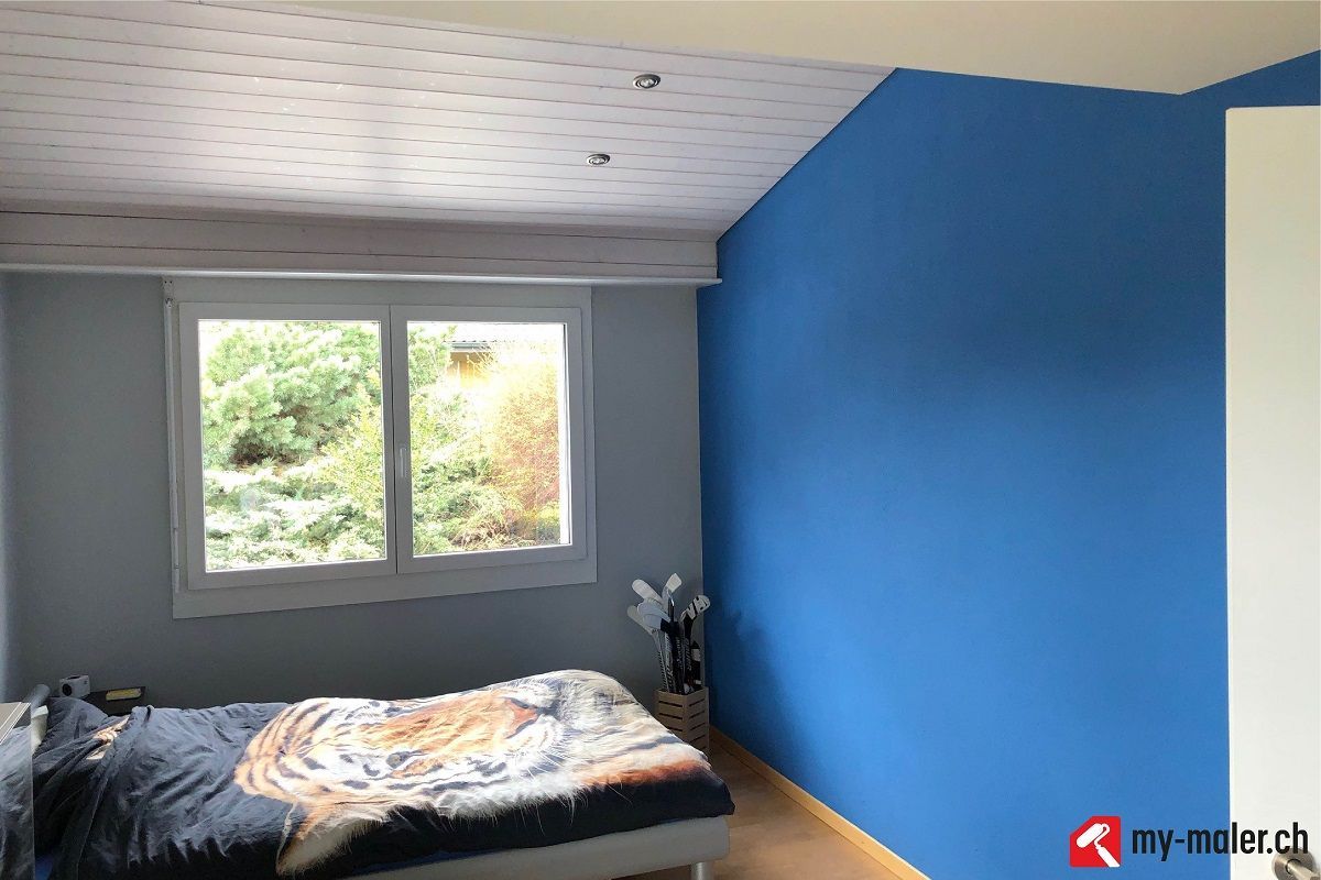 Ein Schlafzimmer mit Bett, Fenster und blauen Wänden.