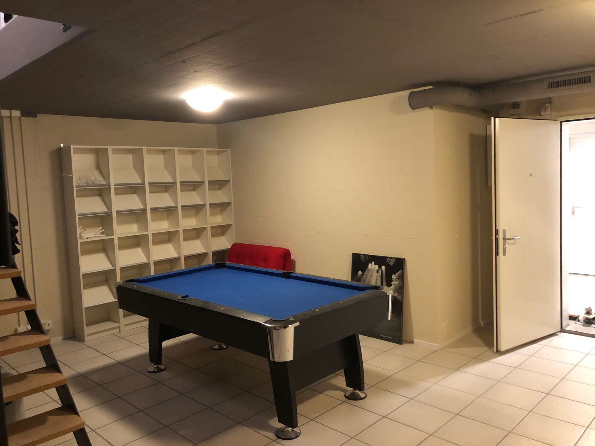 Ein Billardtisch in einem Raum mit Treppen und Regalen