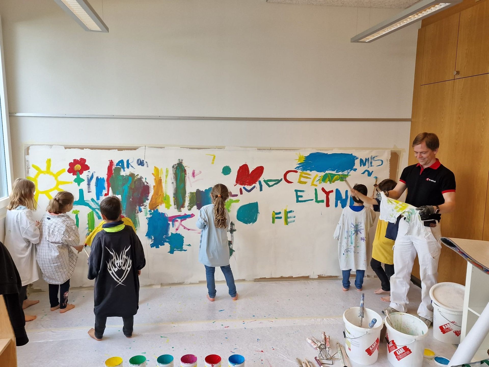 Eine Gruppe Kinder steht vor einer mit Farbe bedeckten Wand.