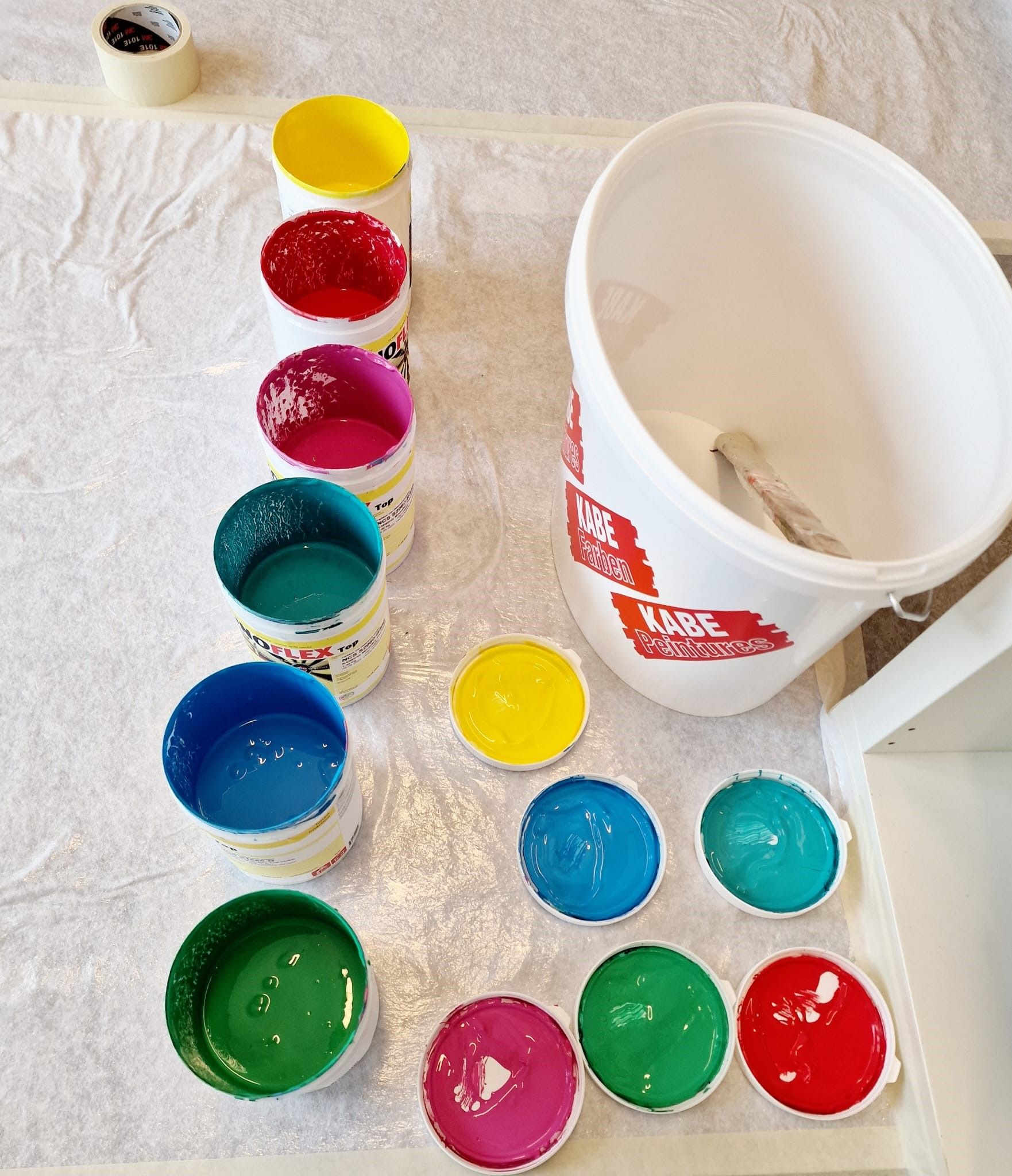 Ein Eimer Farbe steht neben einer Reihe von Bechern mit Farbe