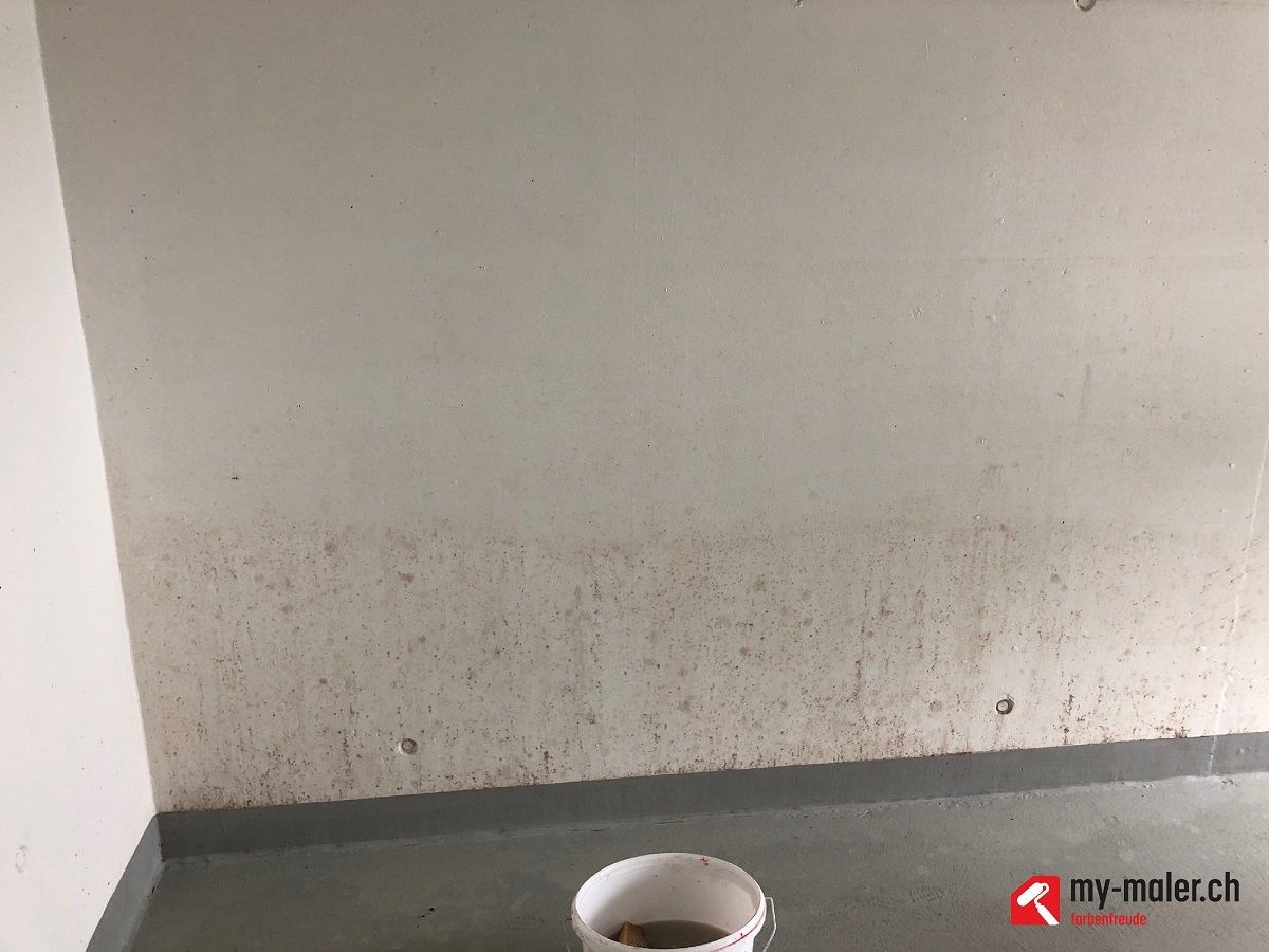 Vor einer Wand steht ein Eimer Wasser auf dem Boden.