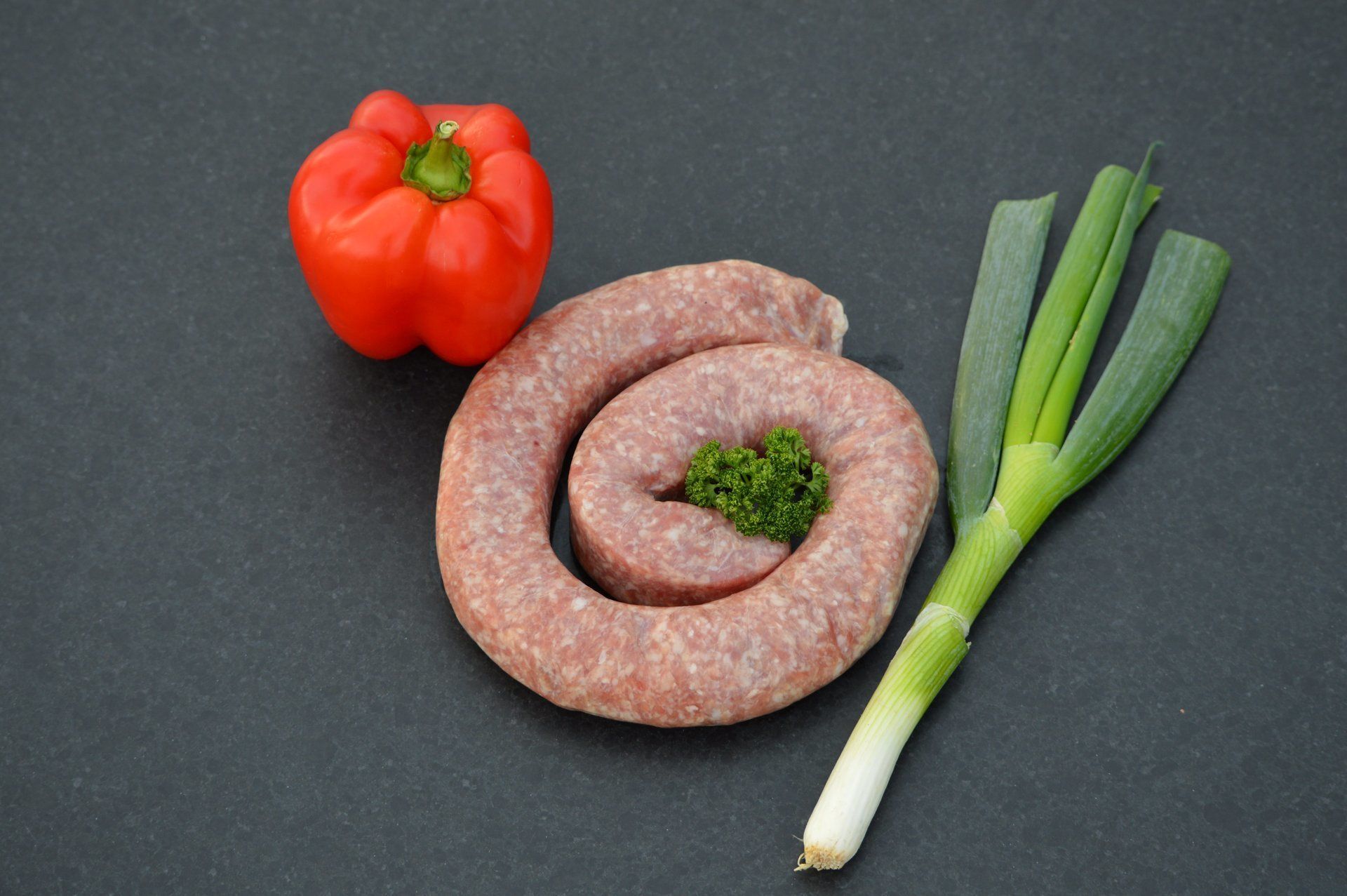 Opgerolde worst, rode paprika en groene uien op een donker oppervlak.