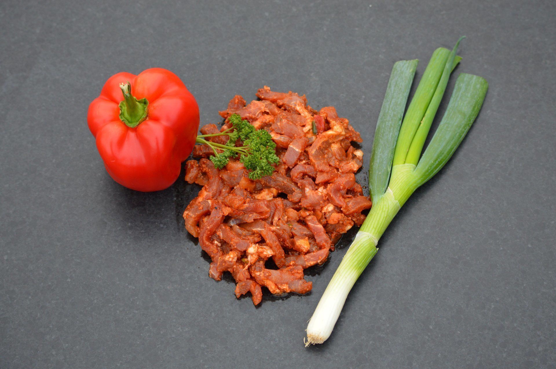 Rode paprika, gehakt en groene ui op een donker oppervlak.