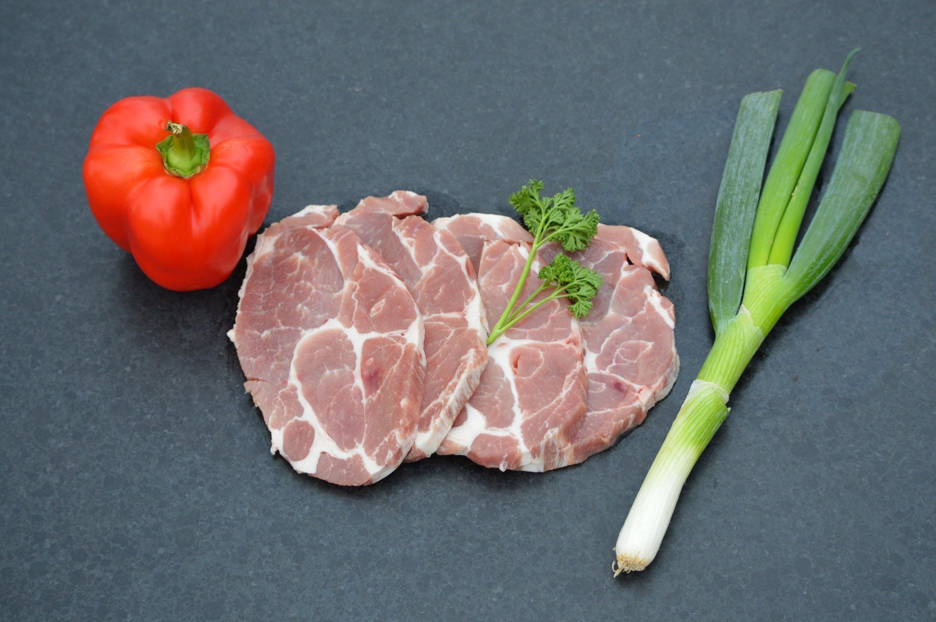 Gesneden varkenslapjes met rode paprika, groene ui en peterselie.