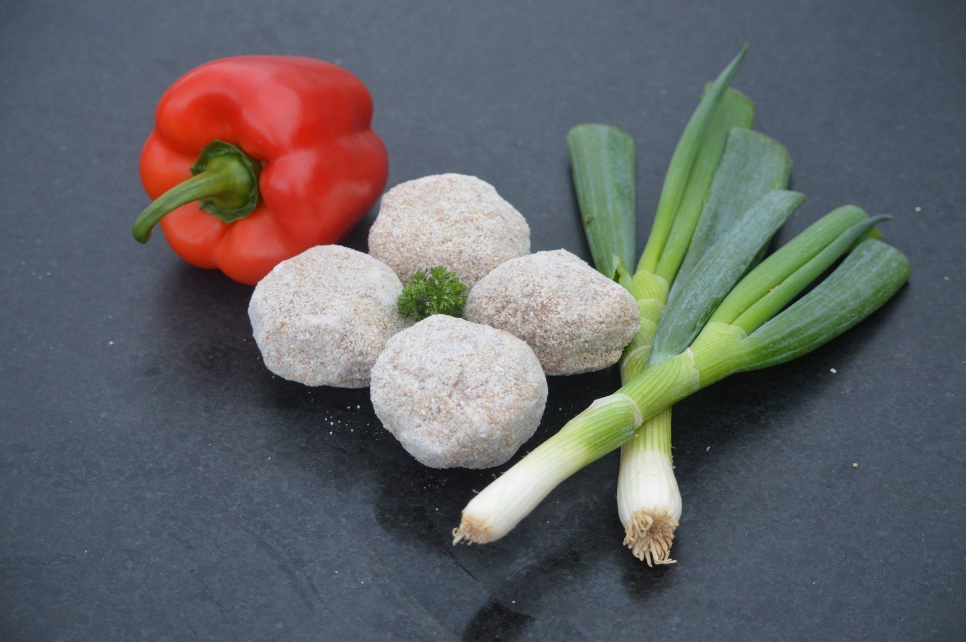 Rode paprika, vier ronde items, groene uien op een donker oppervlak.