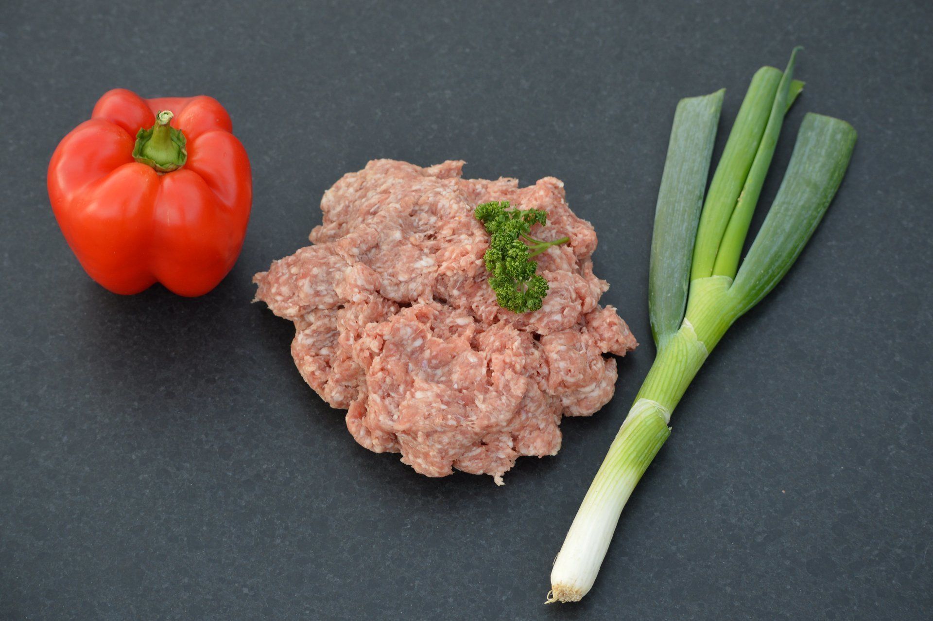 Rode paprika, gehakt en groene uien op een donker oppervlak.