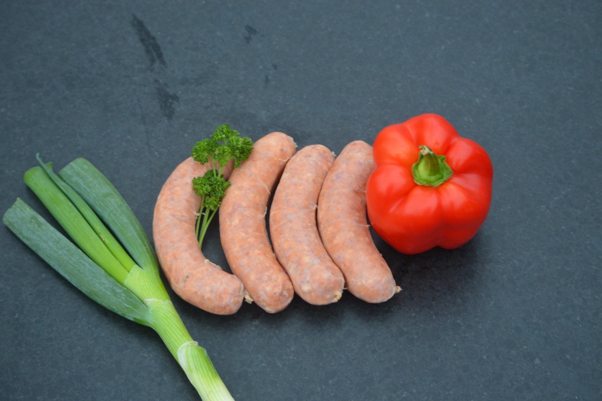 Worstjes, rode paprika en groene uien op een donker oppervlak.