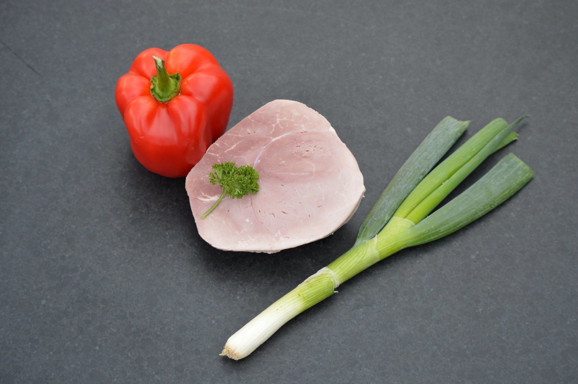 Rode paprika, plakje vlees en groene ui op een donker oppervlak.