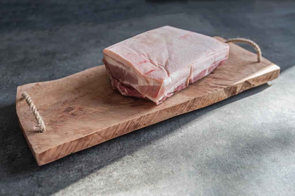 Buikspek op een houten snijplank met touwgrepen, op een donker aanrechtblad.