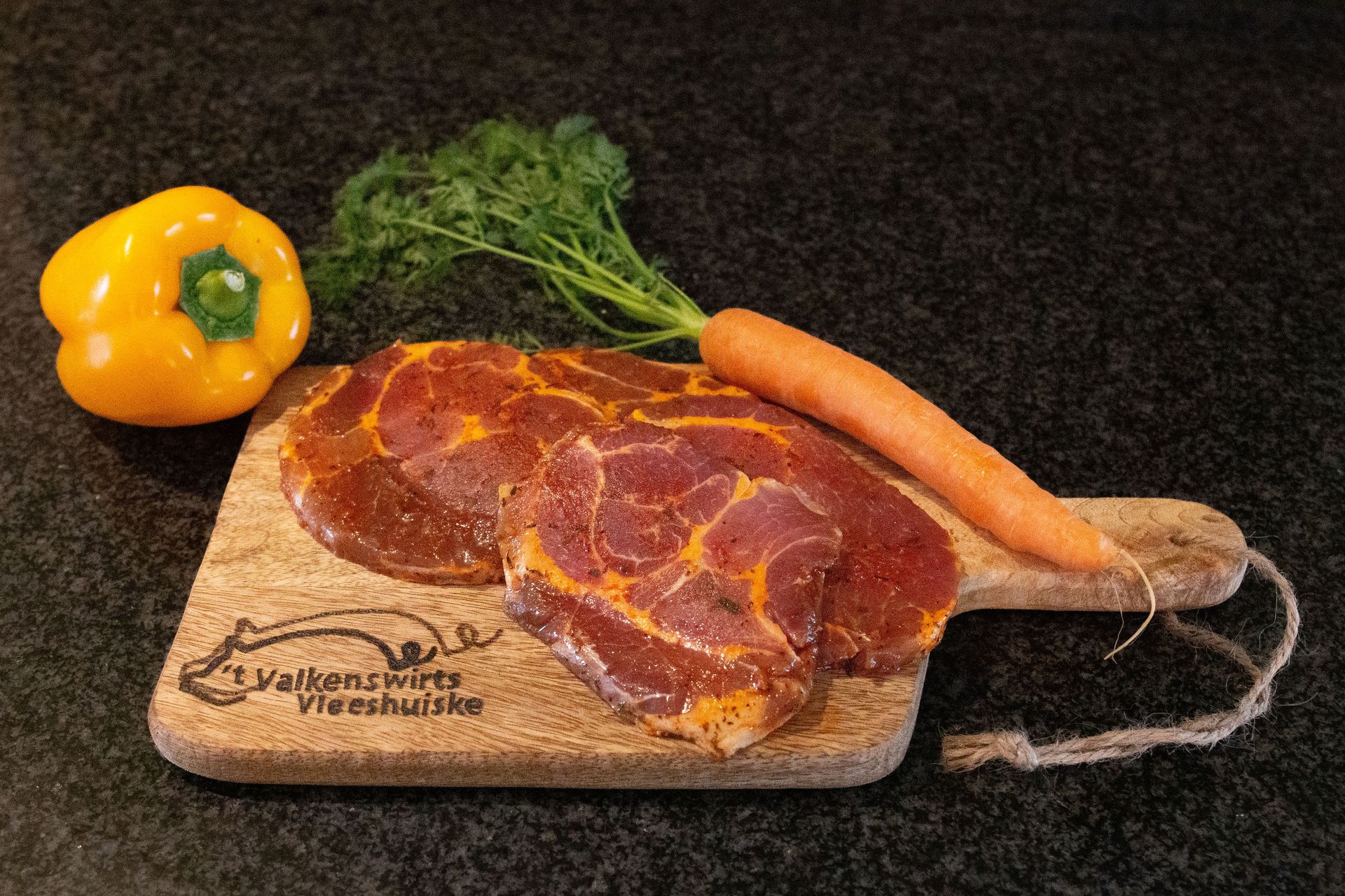 Rauw, gekruid vlees in plakjes op een houten plank met een gele paprika, wortel en peterselie.