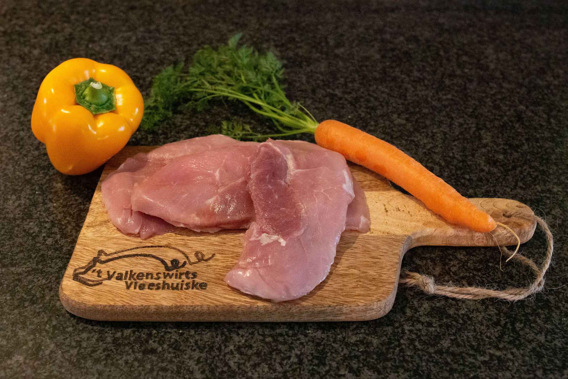 Rauwe kalkoenfilets op een houten snijplank met gele paprika, wortel en dille.