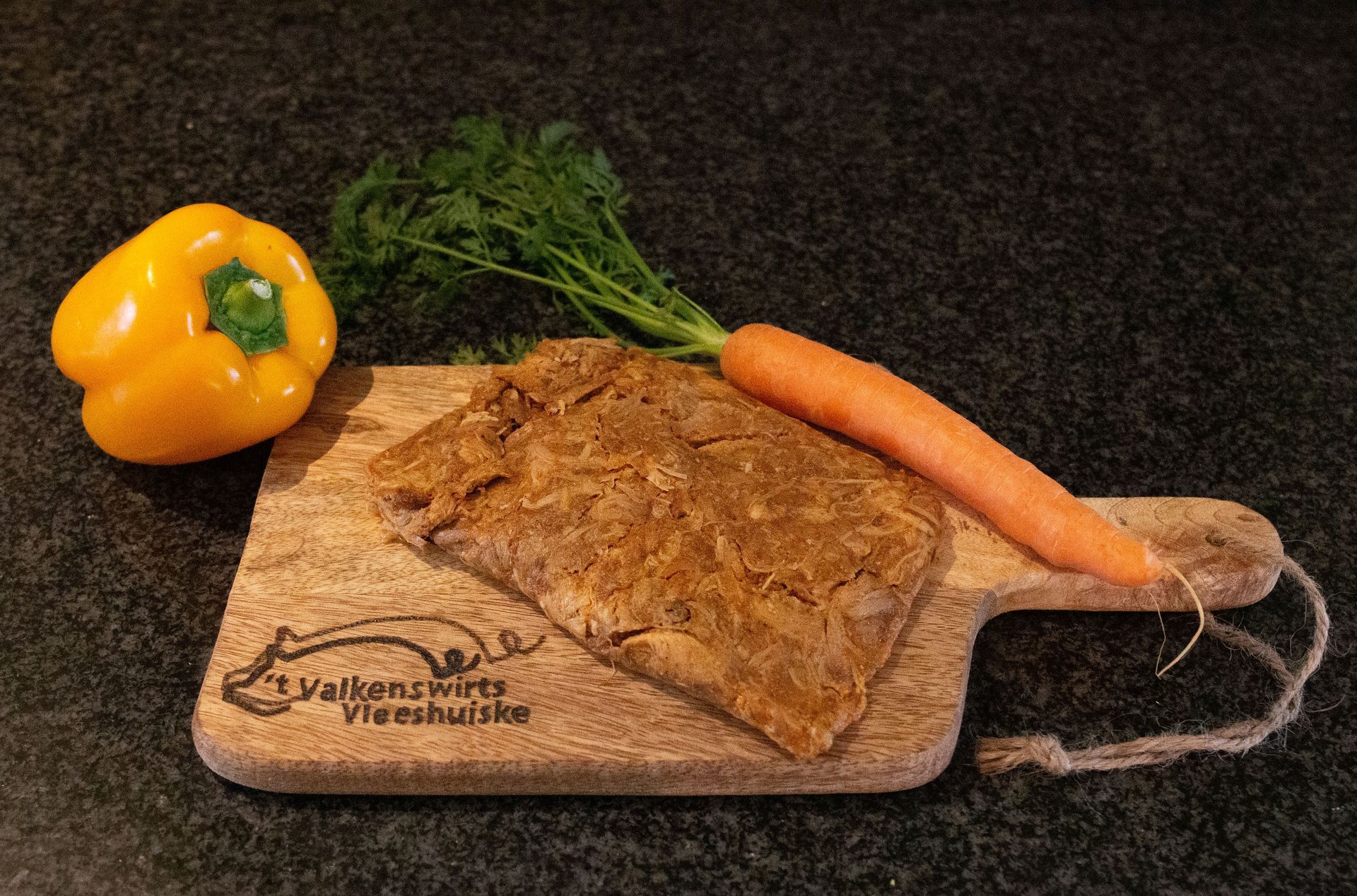 Gele paprika, wortel en een stuk vlees op een houten snijplank.