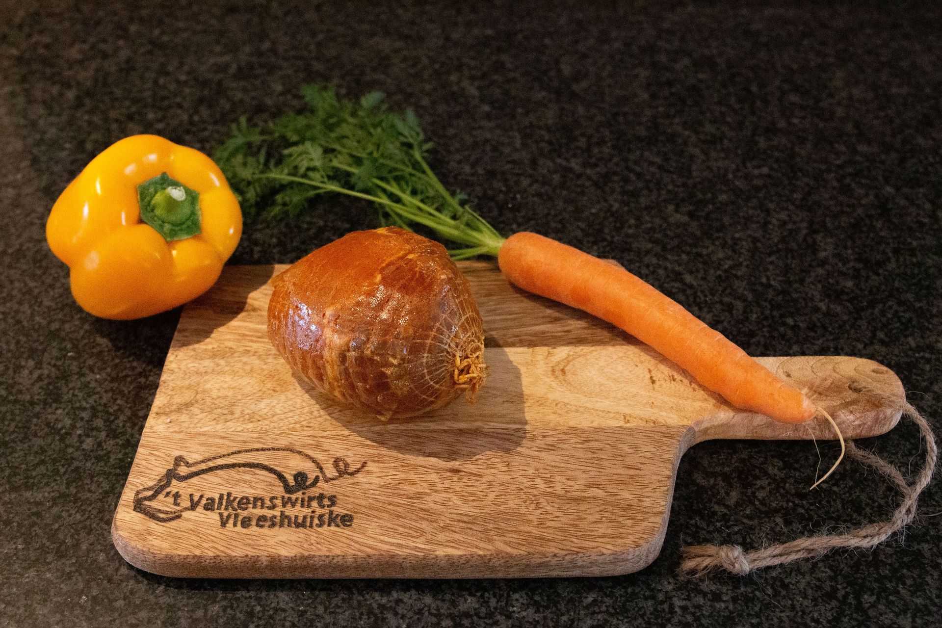 Gele paprika, wortel en een stuk gekookt vlees op een houten snijplank.