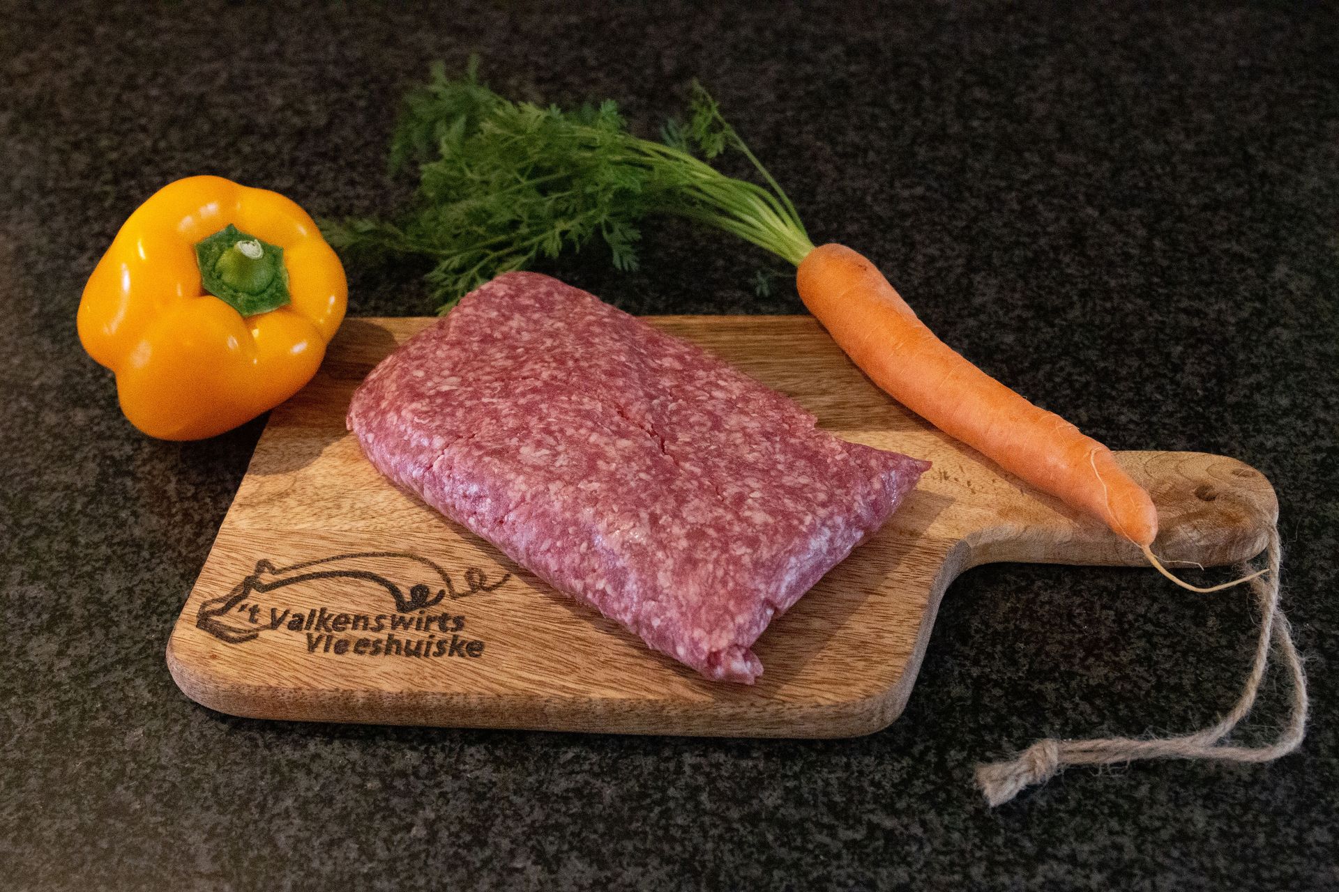 Gehakt op een snijplank met gele paprika en wortel.