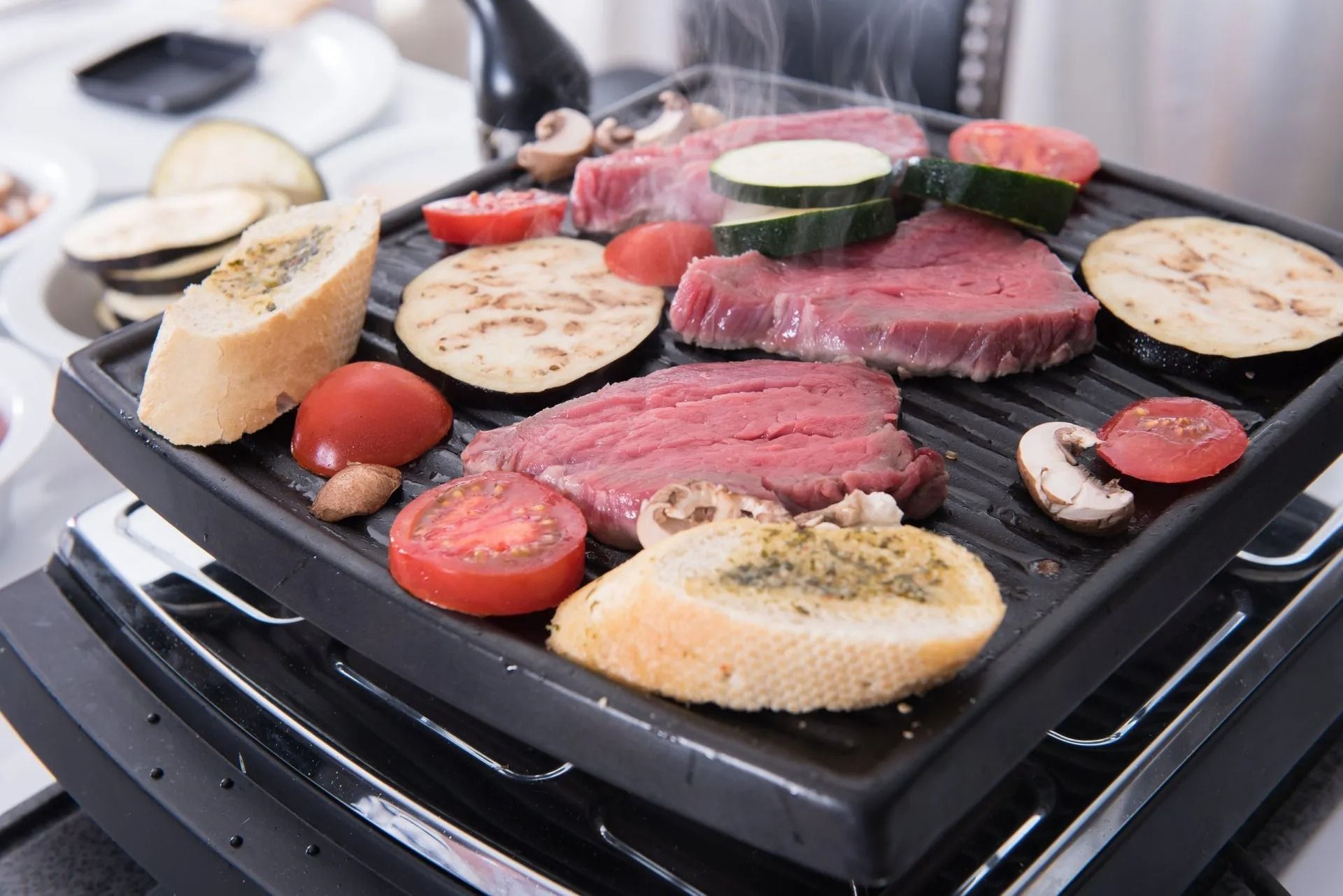 Grillen van biefstuk en groenten op een zwarte elektrische grill. Gesneden brood, tomaten, champignons en courgette.