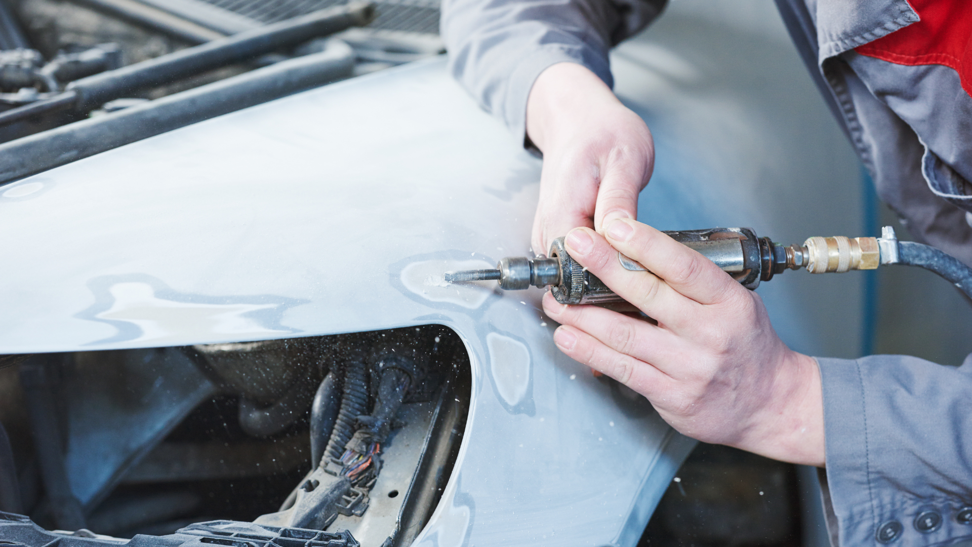 A person using a grinder to repair a car's dented fender.