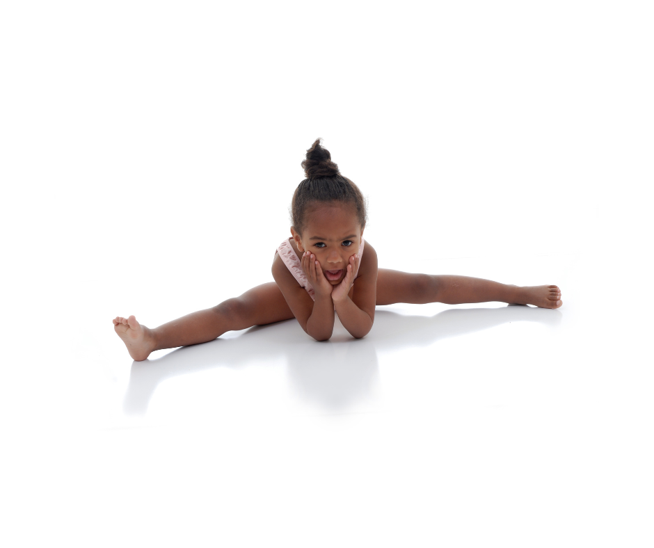 A little girl is laying on the floor doing a split.