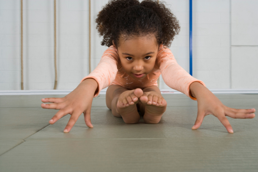 A little girl is stretching her legs on a mat.