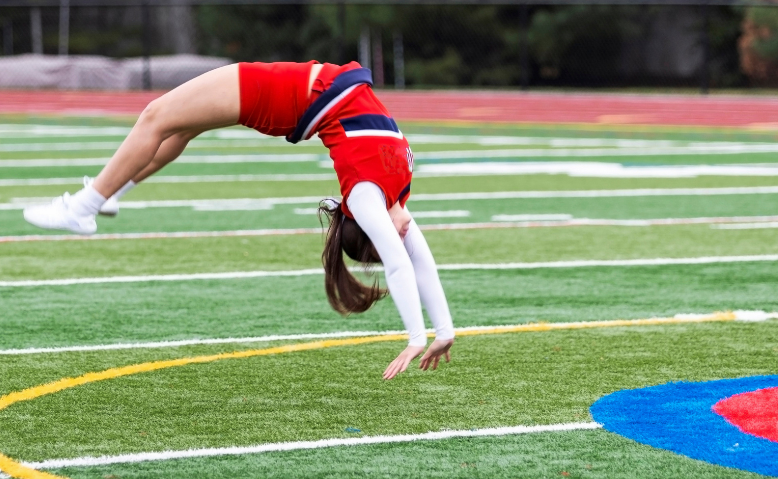 A cheerleader is doing a handstand on a football field.