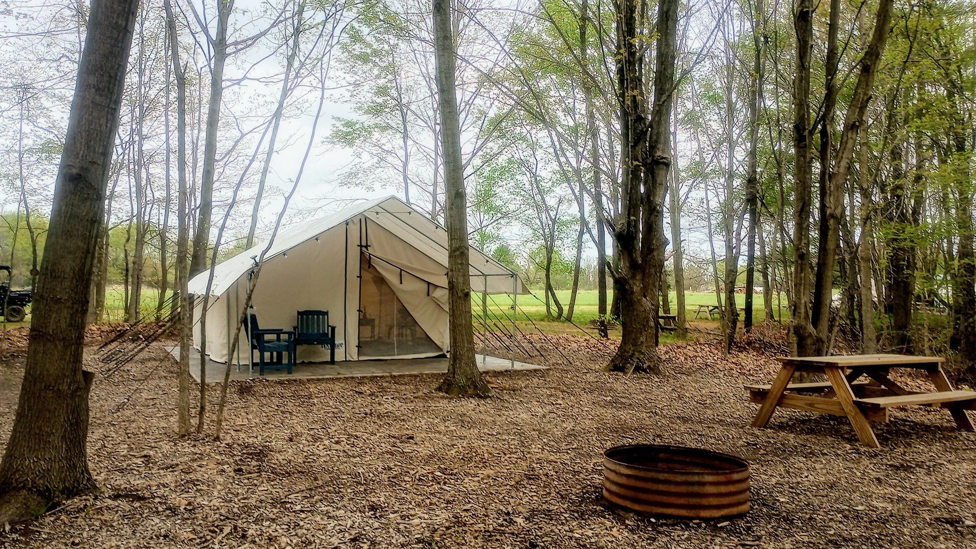 Front view Spruce glamping tent looking across the fire pit and picnic table in the woods.