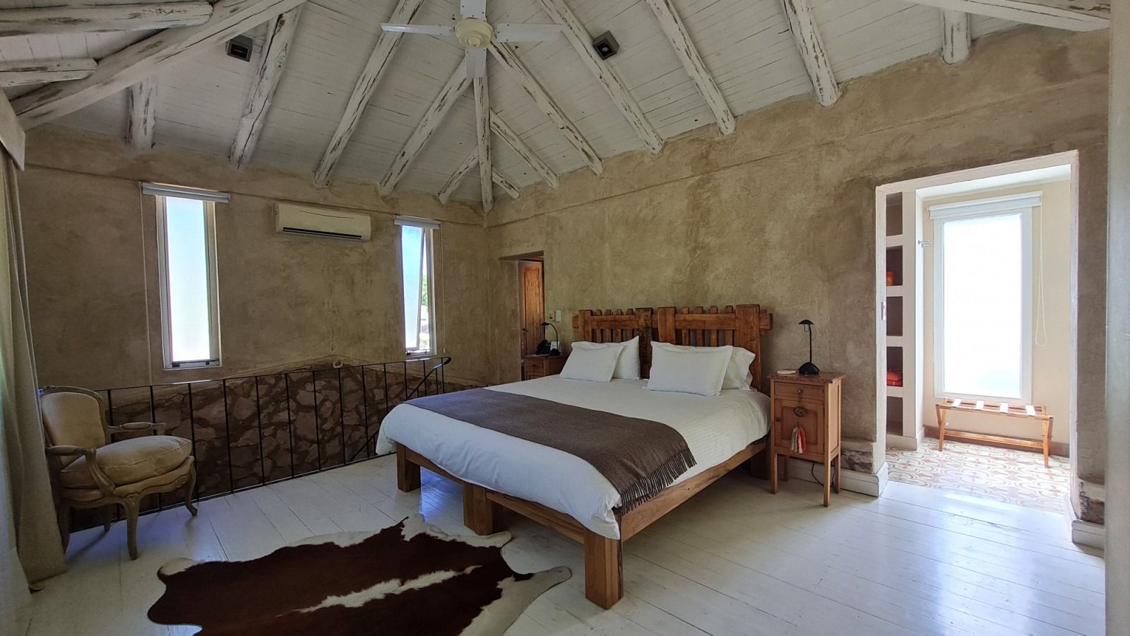 Bedroom with a bed, small windows, tan walls, and a white, vaulted ceiling.