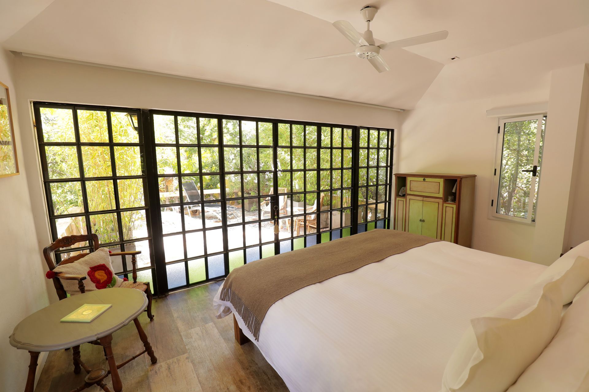 Bedroom with large window overlooking outdoor area; bed, chair, and cabinet.