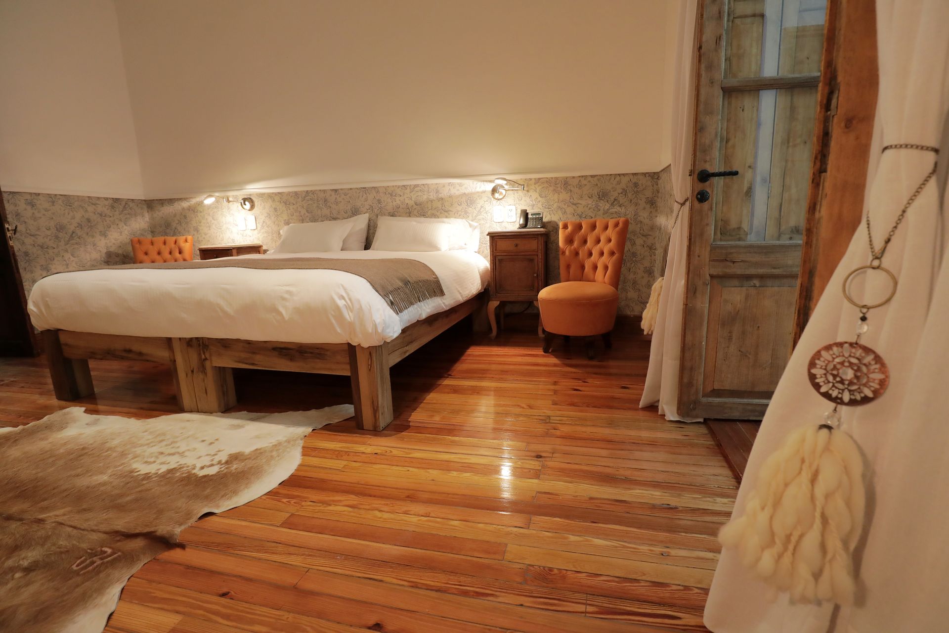 Bedroom with wooden bed, nightstand, and chair, featuring hardwood floors and a decorative curtain.