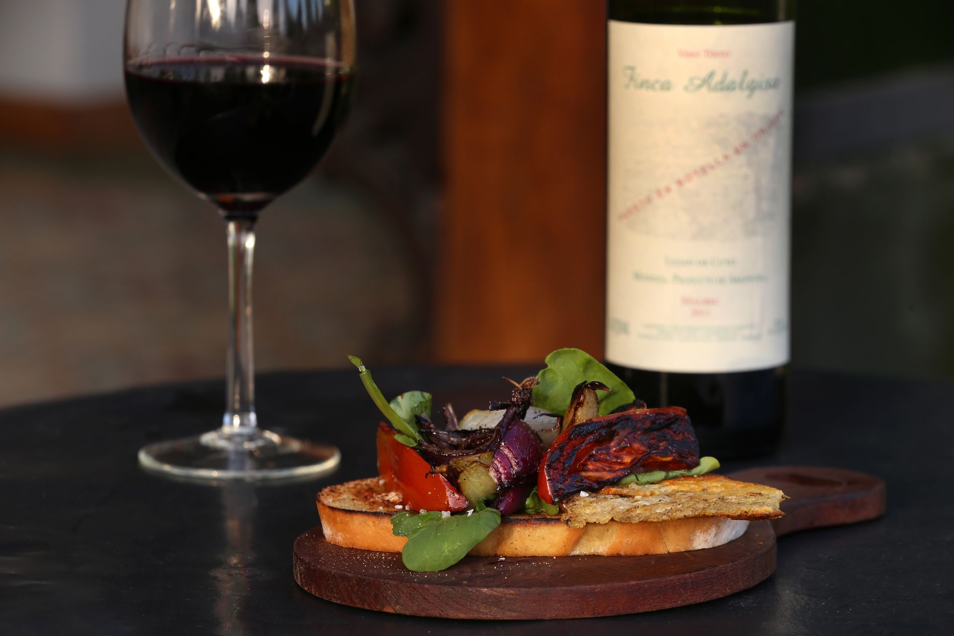 Glass of red wine, appetizer, and bottle of wine on a wooden serving board.