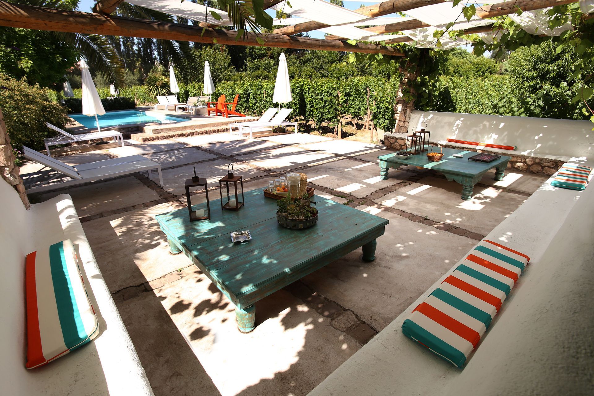 Outdoor patio with turquoise tables, striped cushions, and a pool in the background.