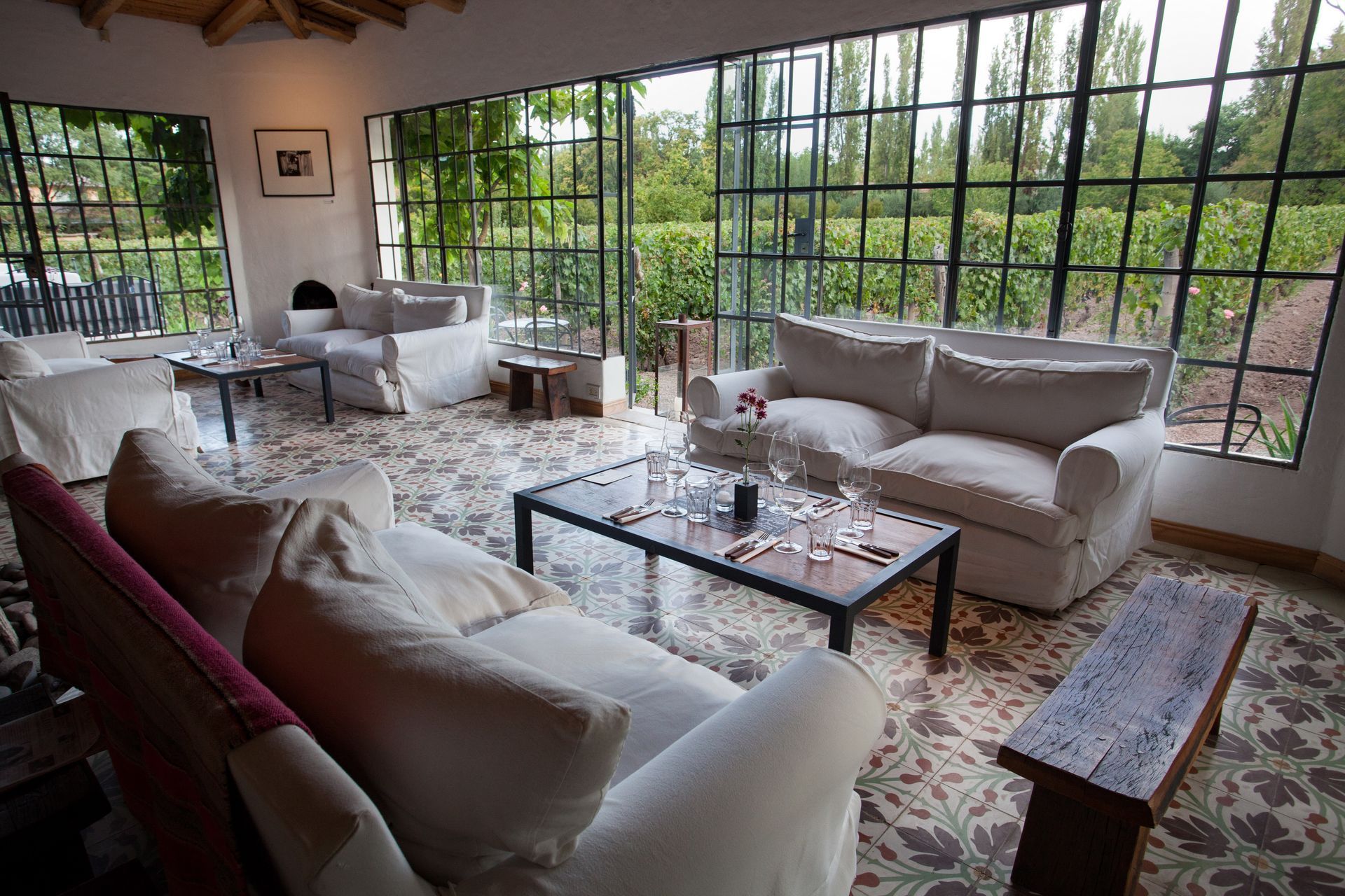 A sunroom with white sofas, a patterned tile floor, and large windows overlooking a vineyard.