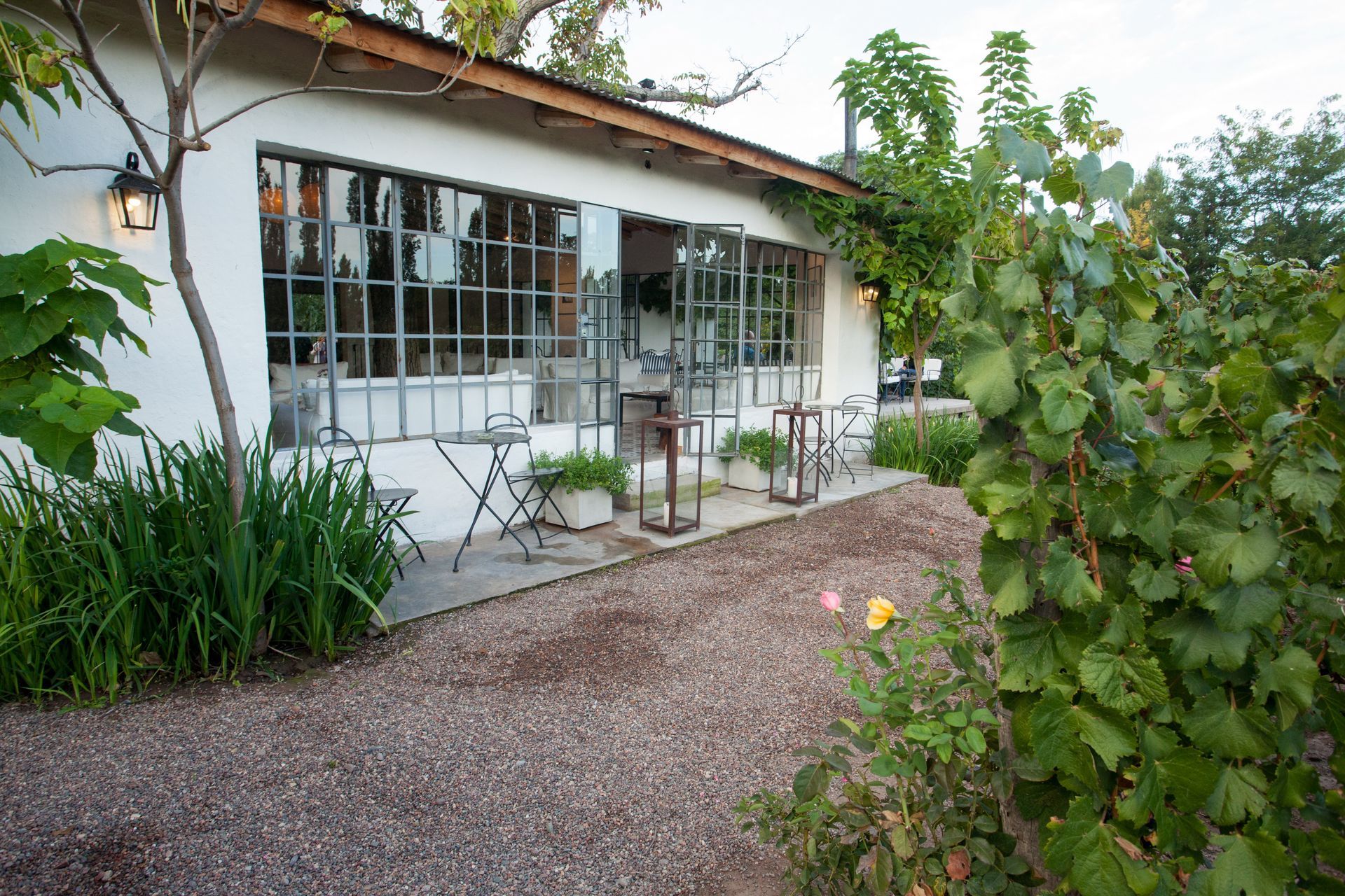 White building with large windows and a gravel pathway, surrounded by greenery.