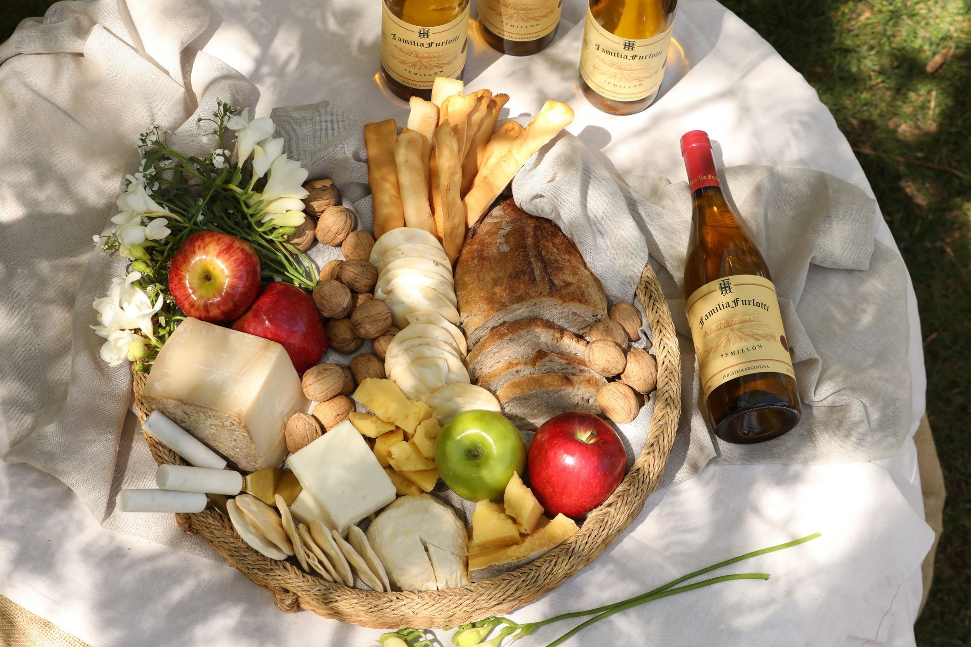 Charcuterie board with cheese, bread, apples, nuts, and wine bottles on a table.