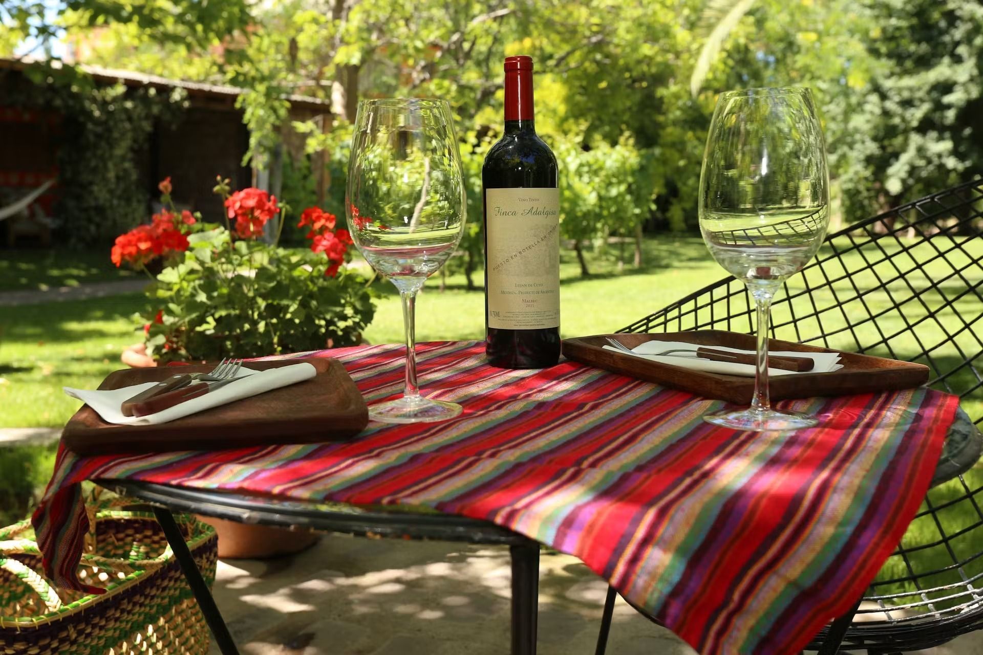 Table set for wine tasting outdoors: bottle, glasses, cigars, red and striped cloth.