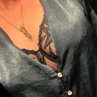Close-up of a dark satin blouse with lace trim and buttons, worn with a gold pendant necklace.