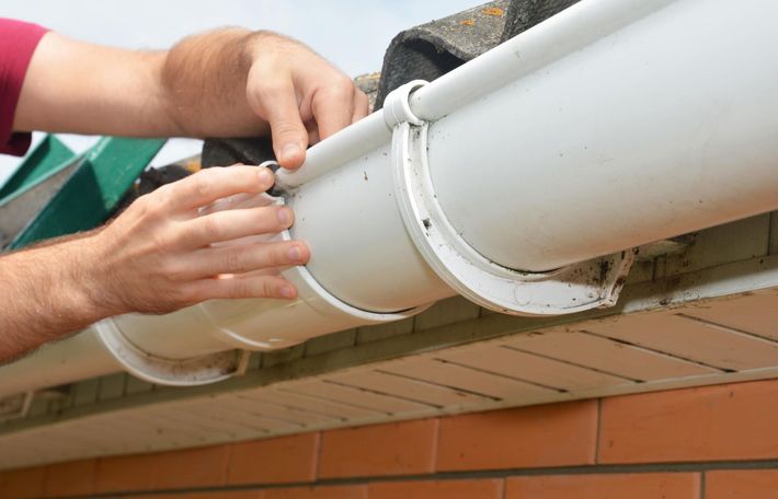 Hands adjusting white gutter on a brick building's roof edge.