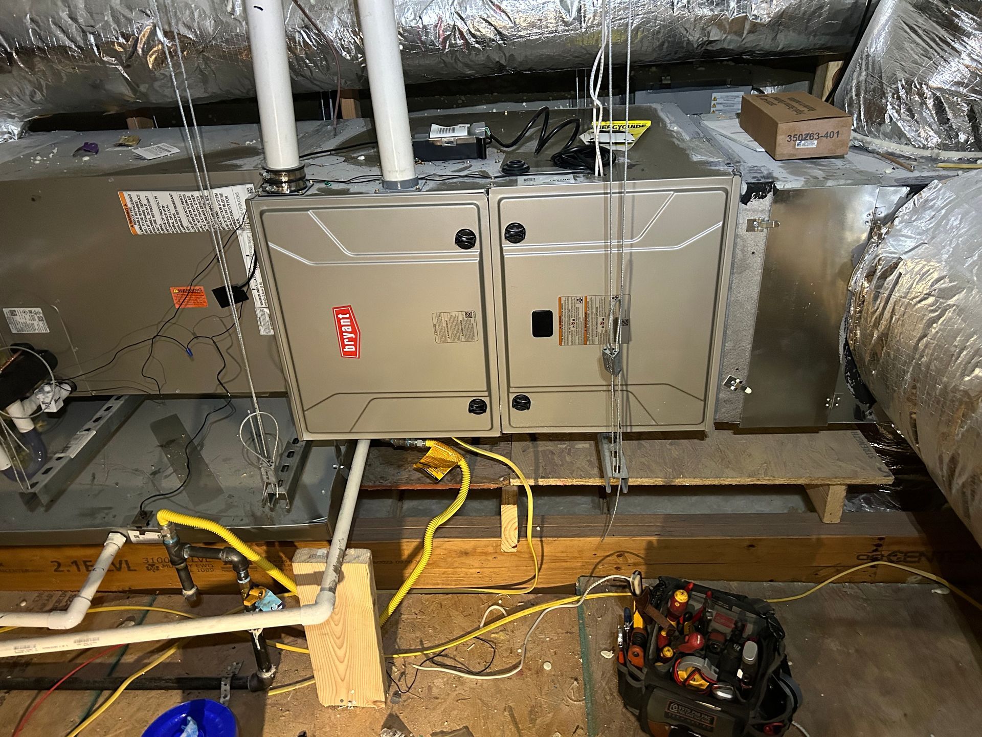 HVAC unit in an attic space with ductwork, electrical wiring, and tools.