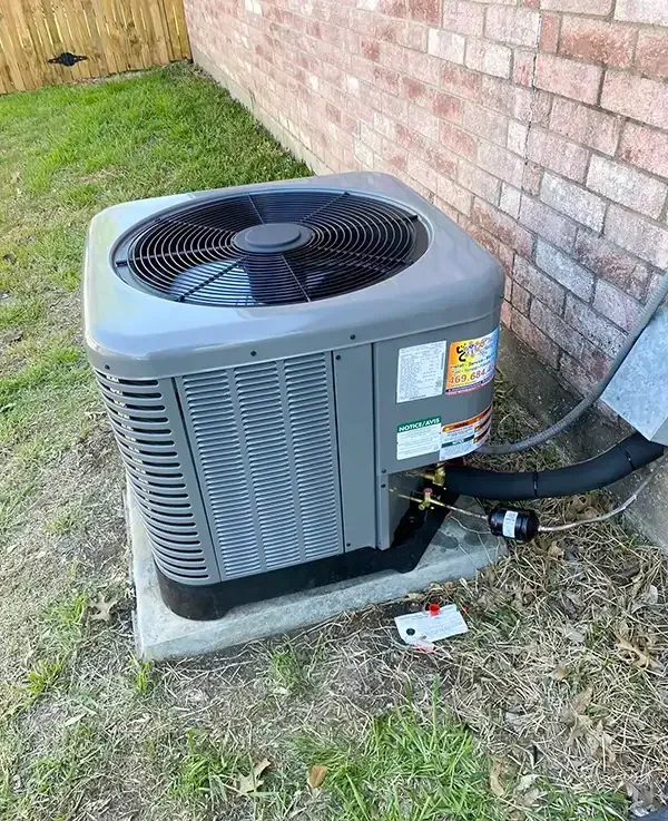 Gray air conditioning unit on a concrete pad next to a brick wall and green grass.