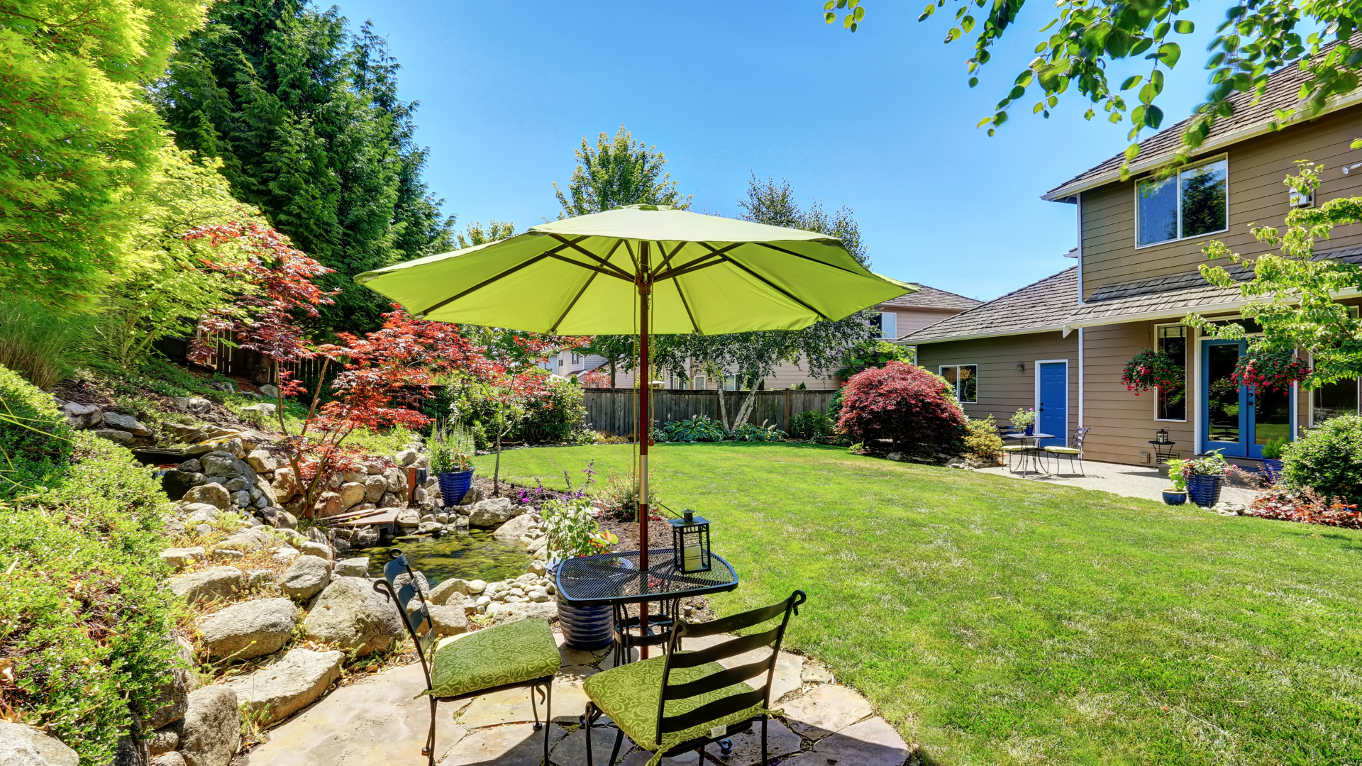 A backyard with a table and chairs under an umbrella.
