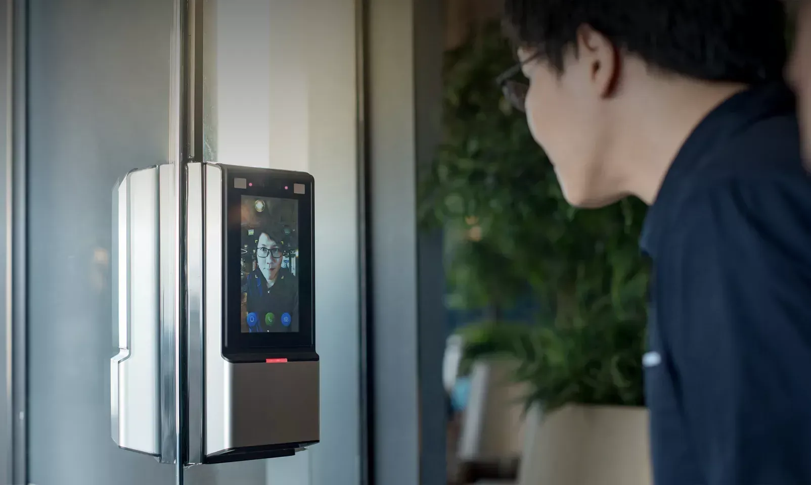 Person using a wall-mounted biometric access scanner with a lit screen indoors.