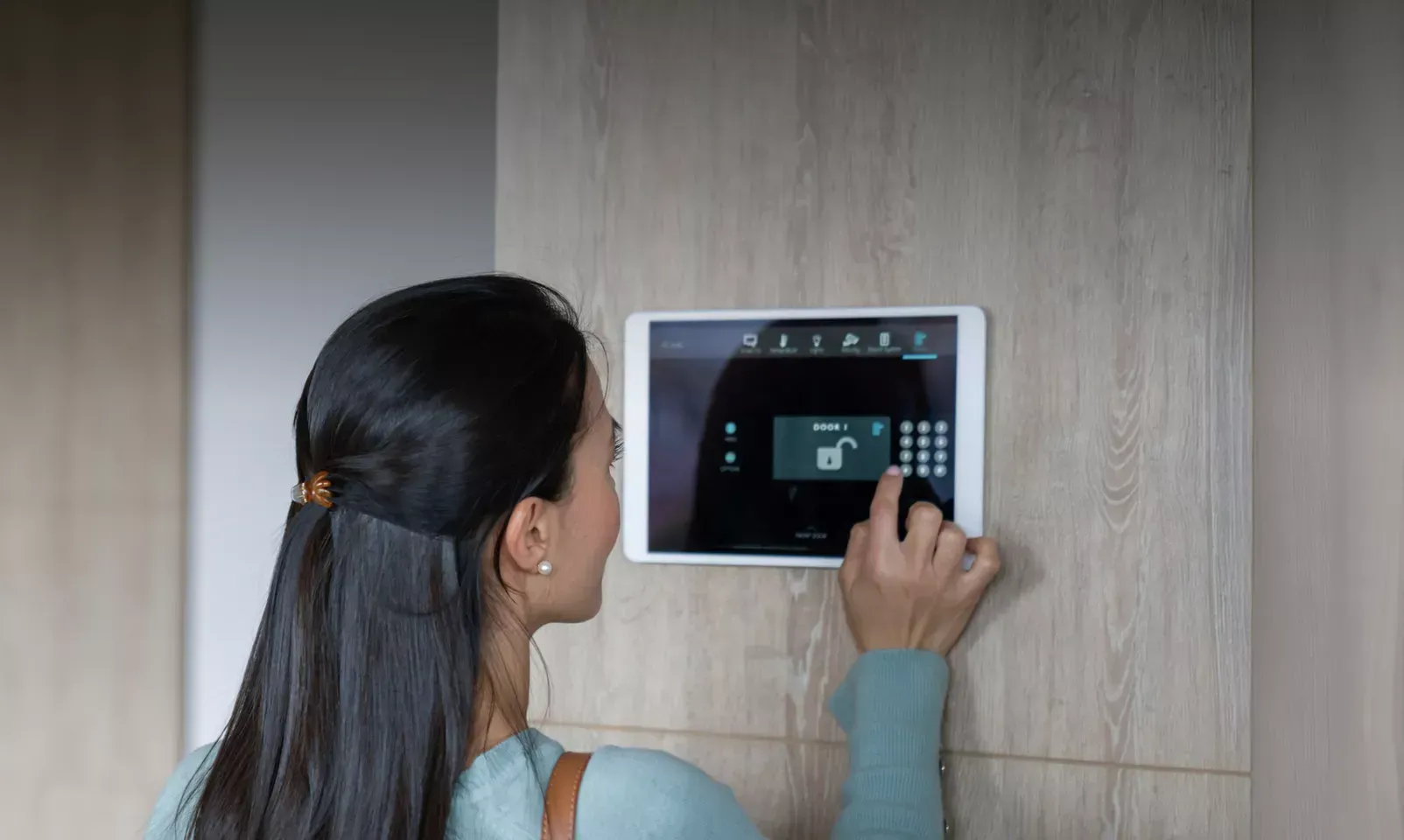 Woman using a wall-mounted touchscreen Intruder alarm control panel.
