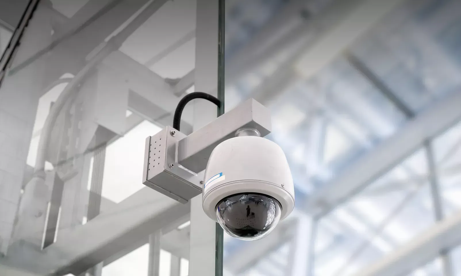 White security camera mounted indoors on a ceiling bracket overlooking a bright modern space