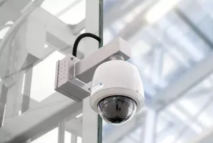 White dome security camera mounted on a ceiling bracket in a bright modern building