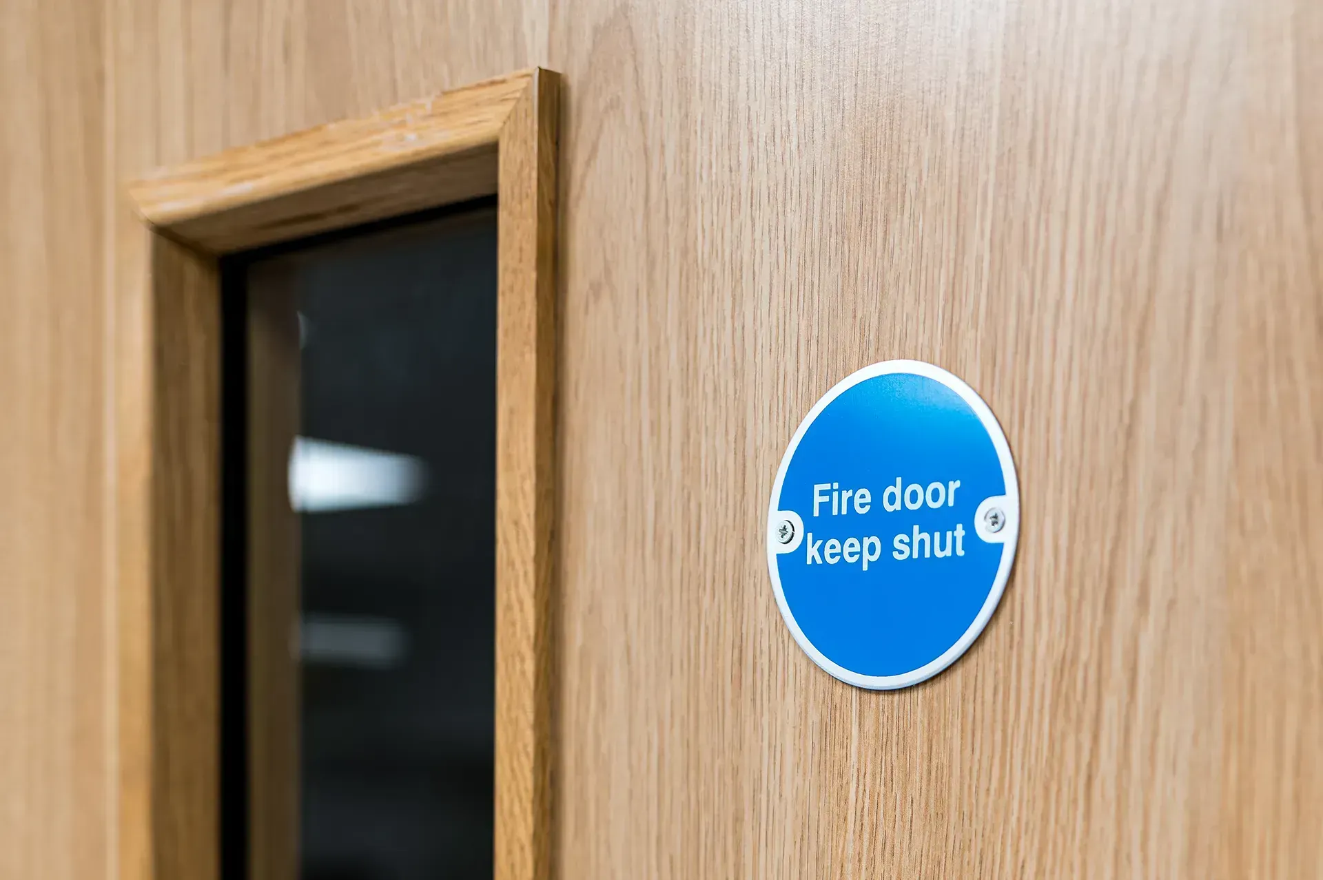 Blue “fire door keep shut” sign on a wooden door with a window panel