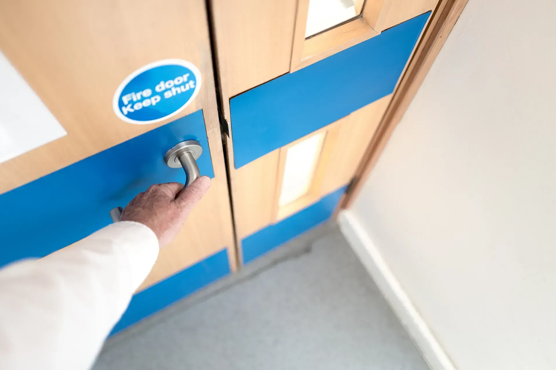 Hand opening a blue door with a push bar in a hallway