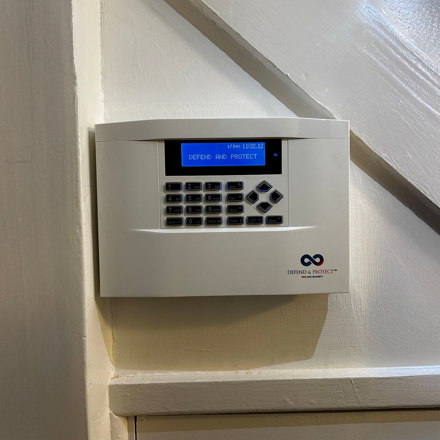 White wall-mounted security keypad with blue display near a staircase。