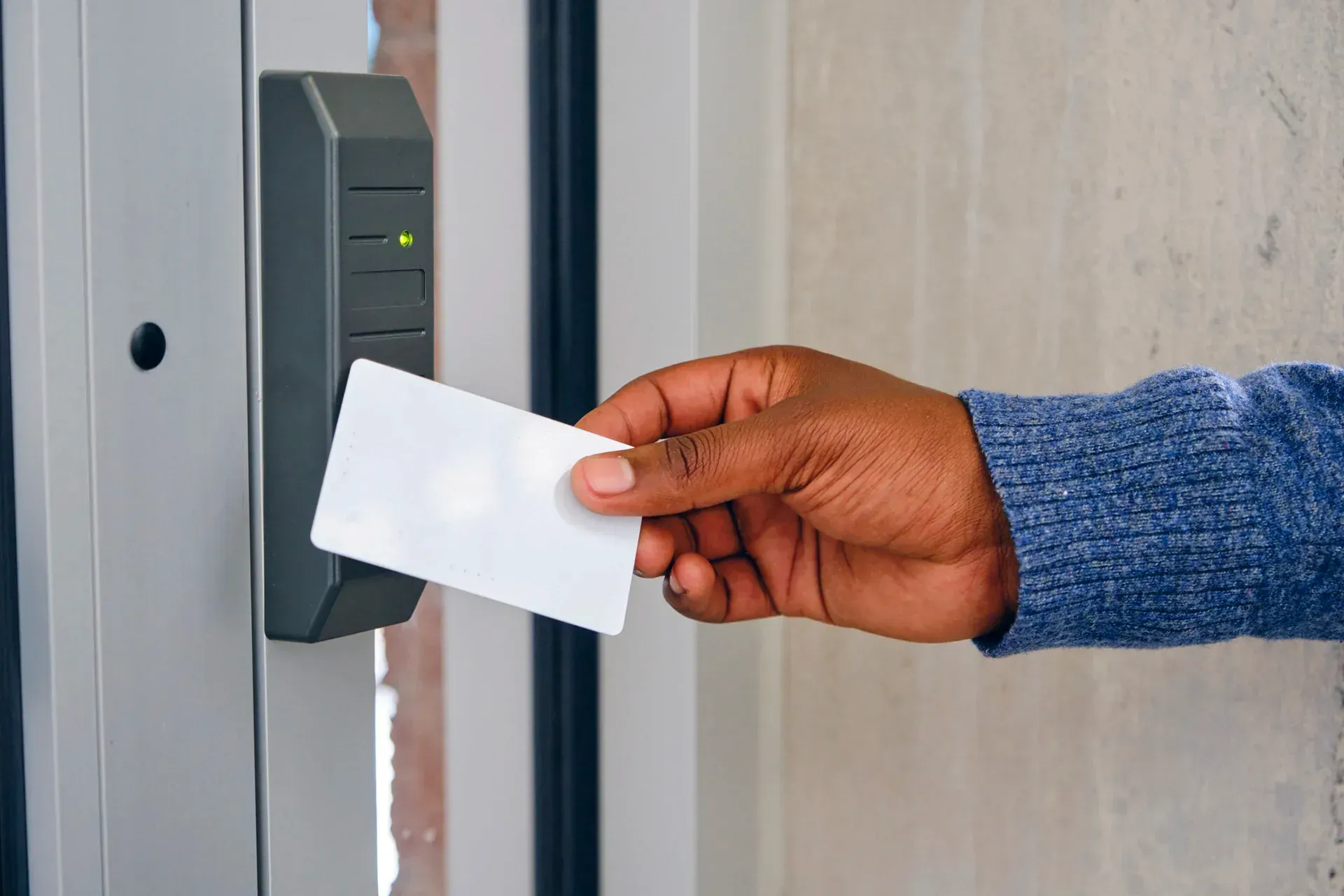 Hand holding a white card up to a security card reader by a door