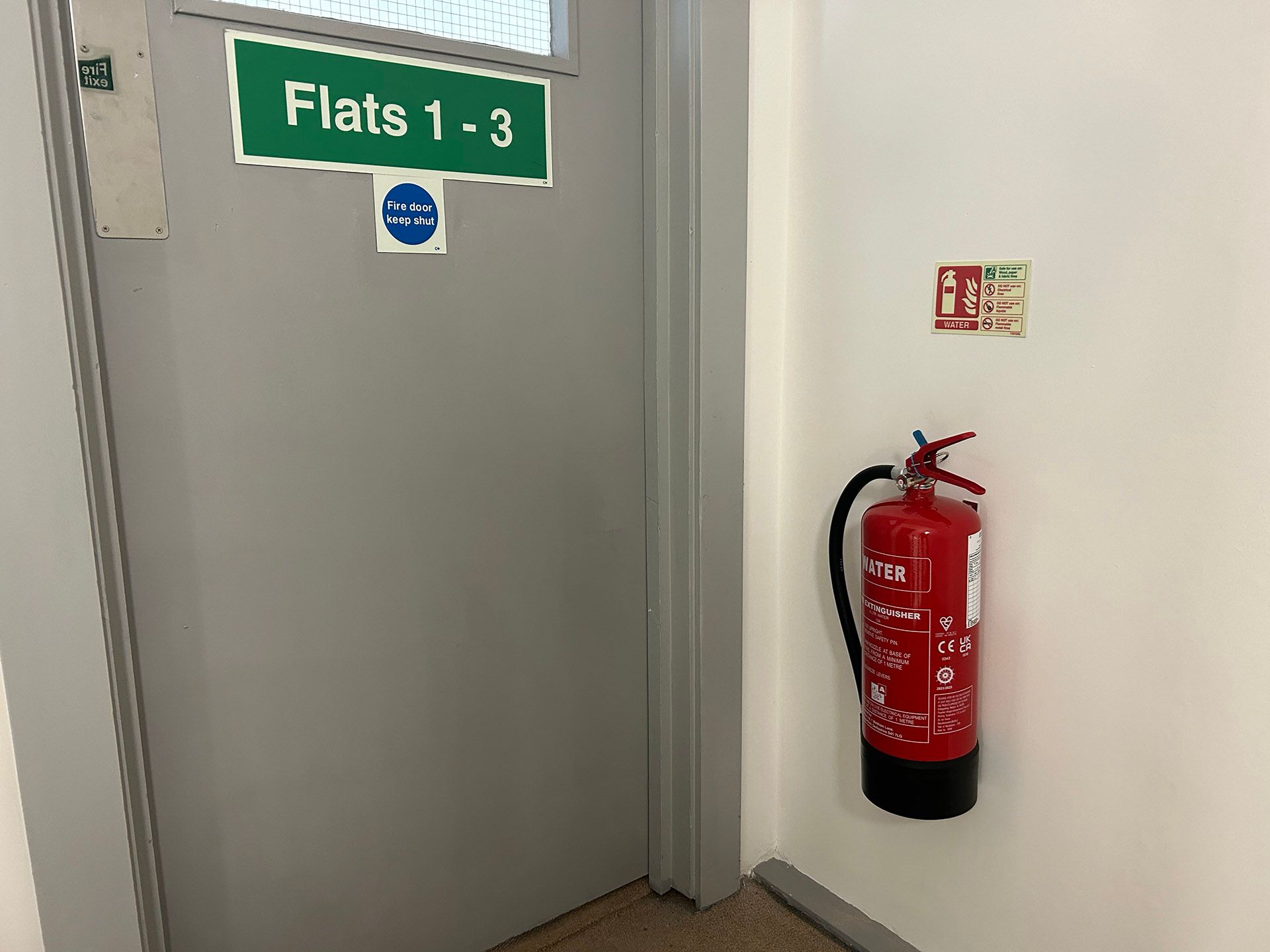 Gray door labeled “Flats 1-3” beside a red fire extinguisher on a white wall.