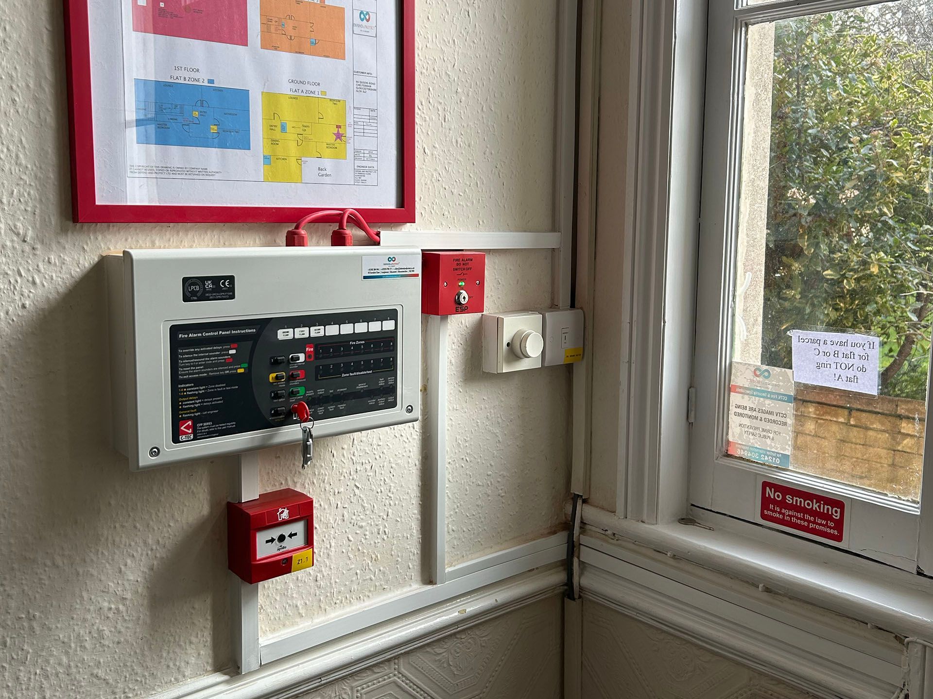 Wall-mounted emergency control panel and alarm boxes beside a window in a utility room